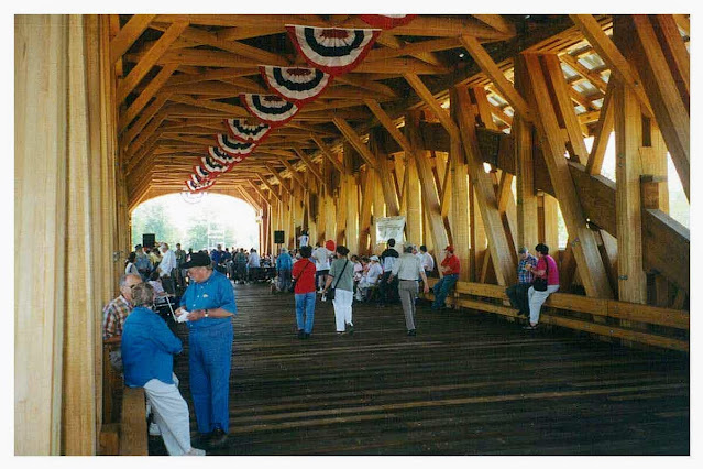 People walking on a wooden covered bridge on the 4th of July with lots of red white and blue banners and bunting.