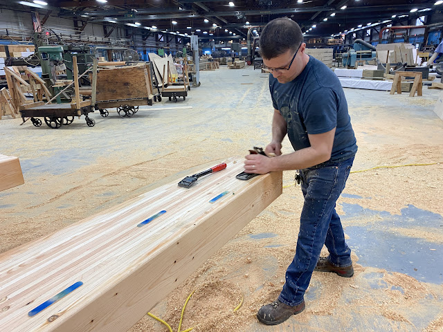 A worker smoothes a beam after filling holes and imperfections.