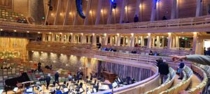 Interior view of a wooden auditorium with spectators and stage setup for a performance.