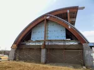 Curved wooden construction beams with scaffolding and a building under construction.