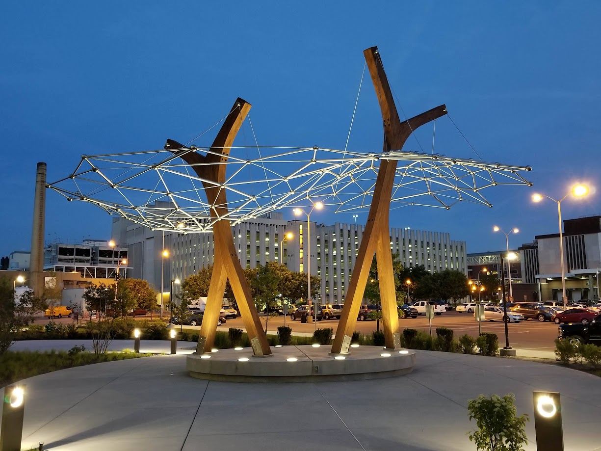 Artistic wood beam structure at night with a city backdrop and lights.