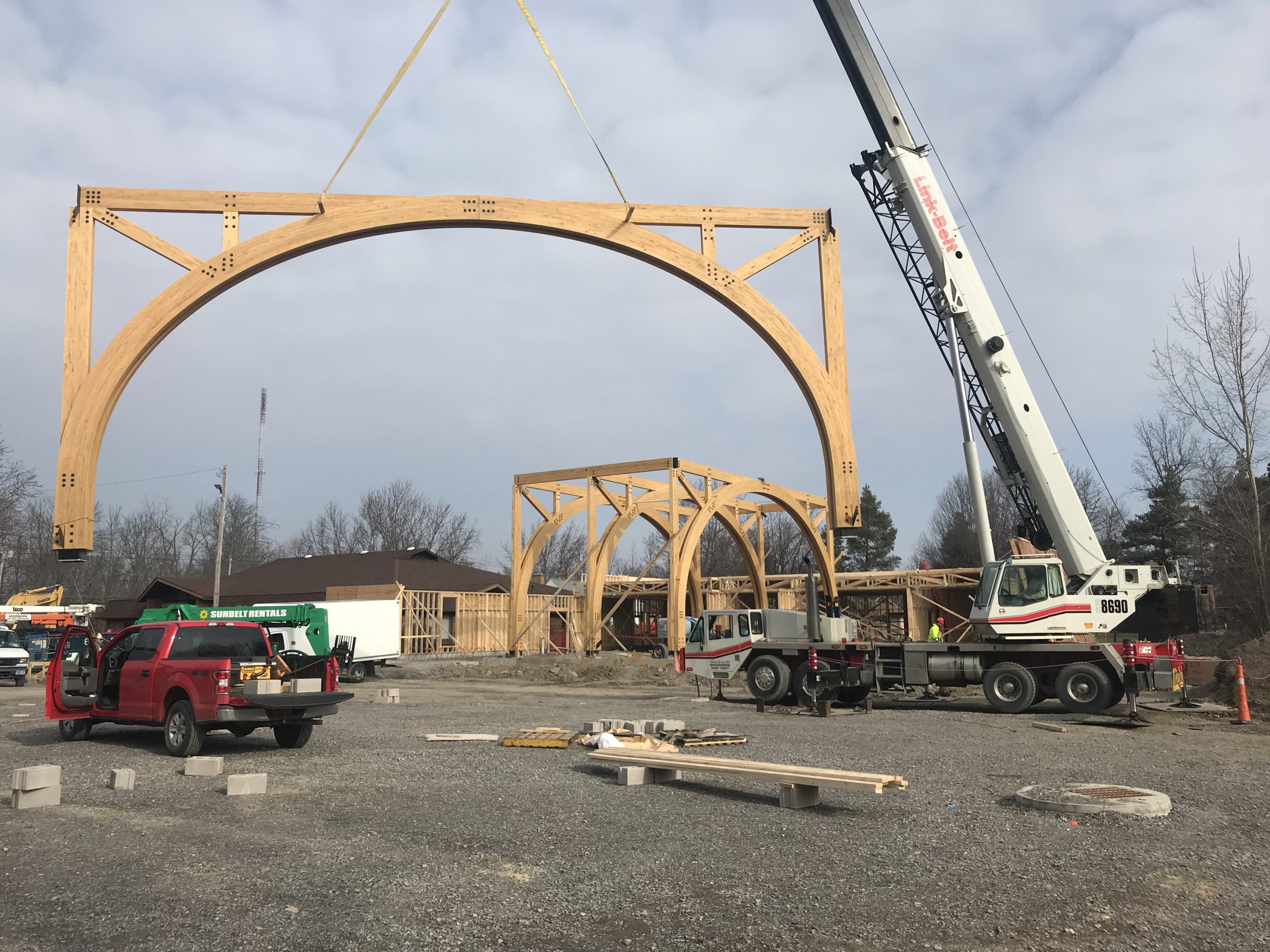 Cranes lifting laminated wood beams for Unalam construction site.