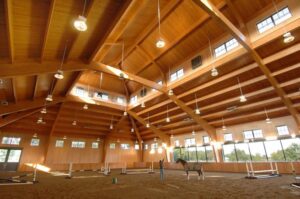 Wood laminate beams in a spacious indoor riding arena with a horse and rider.