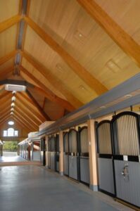Interior of a barn featuring wood laminate beams and horse stalls by Unalam.